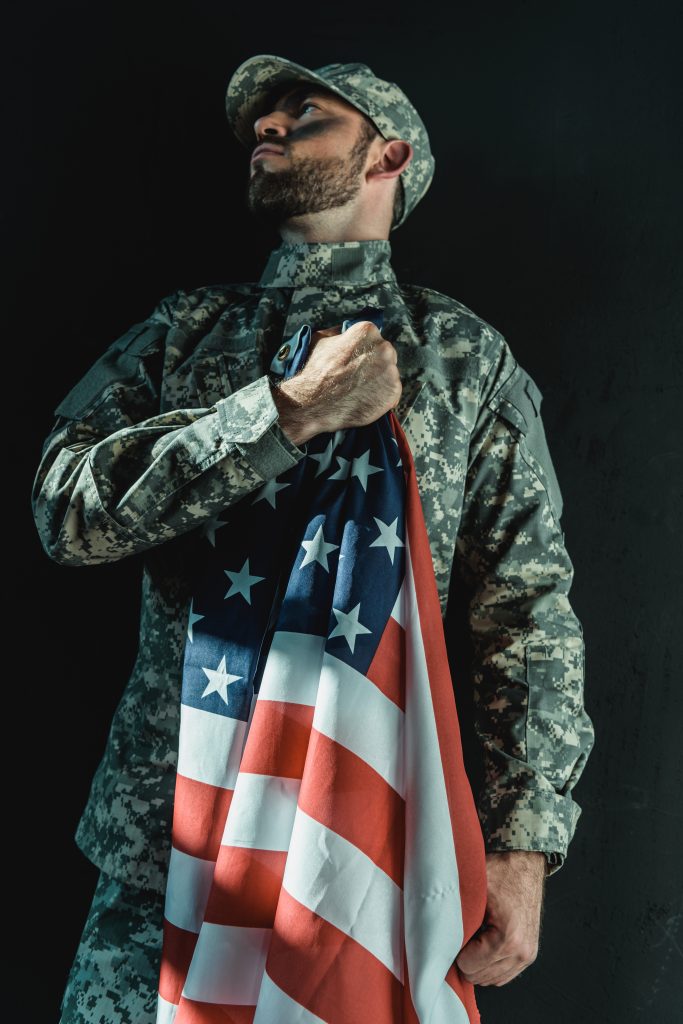 soldier holding united states flag on heart isolated on black